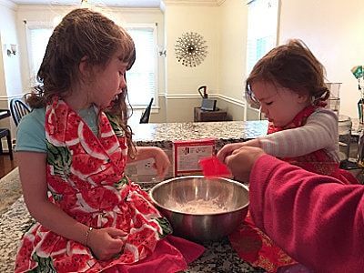 Two little girls are sitting on a counter mixing ingredients in a bowl.