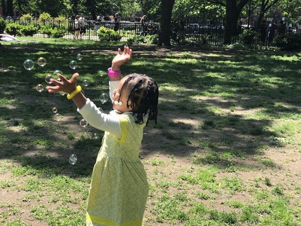 A little girl in a yellow dress is playing with soap bubbles in a park.