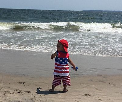 A little boy in an american flag outfit is standing on the beach