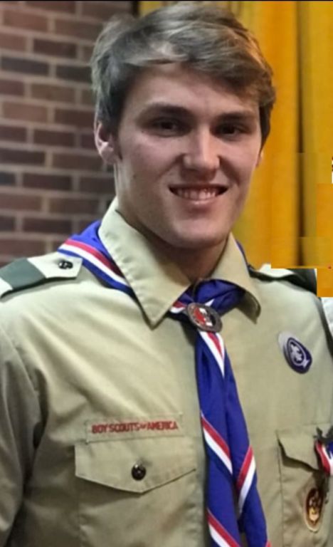 A young man in a boy scout uniform is smiling for the camera.