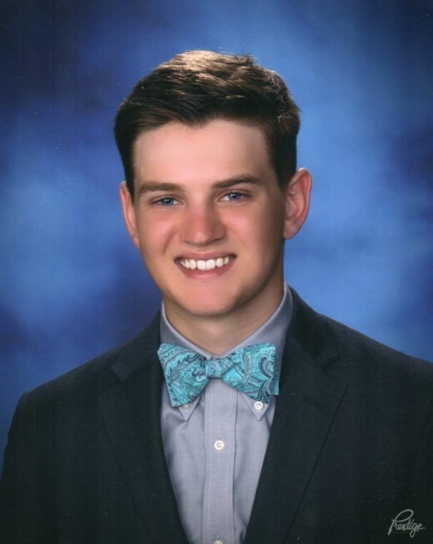 A young man in a suit and bow tie smiles for the camera