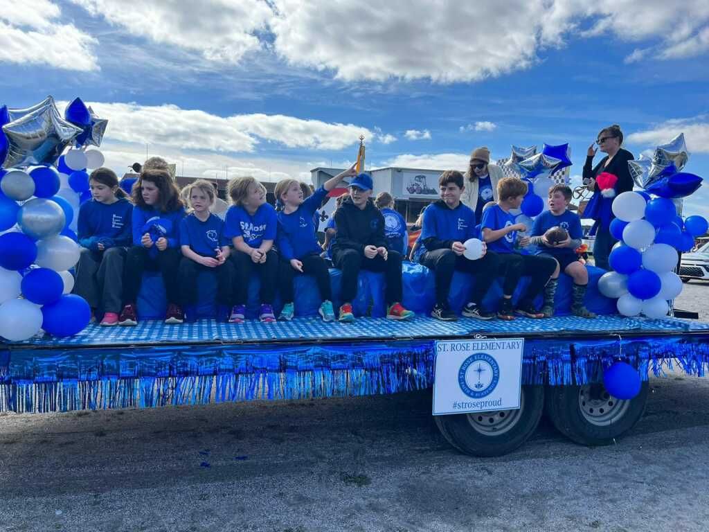 A group of children are sitting on top of a float decorated with blue and white balloons.