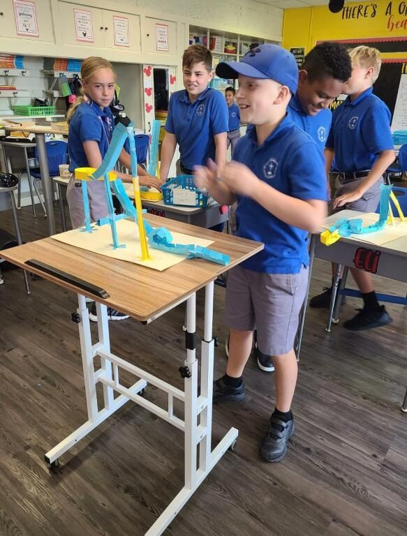 A group of children are standing around a table with a model of a windmill on it.