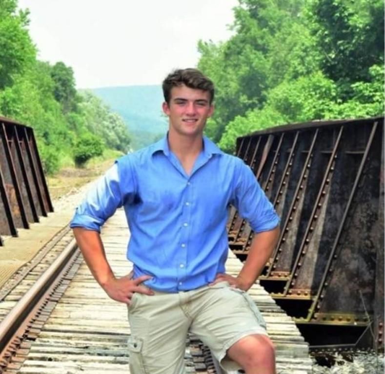 A man in a blue shirt and khaki shorts stands on train tracks