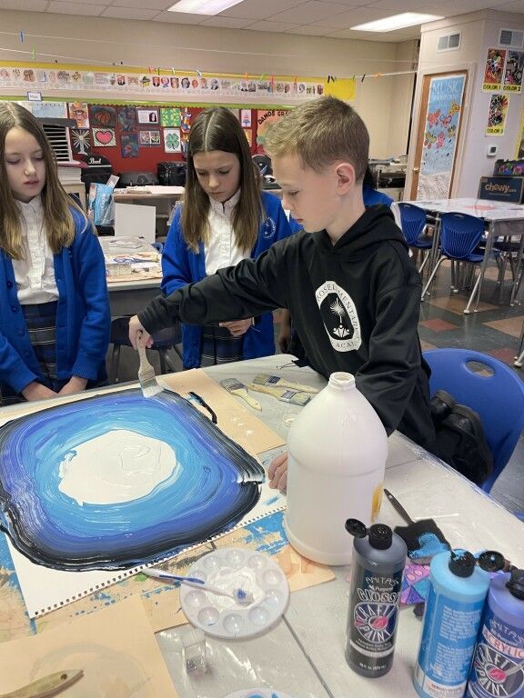 A boy is painting a picture in a classroom with other children