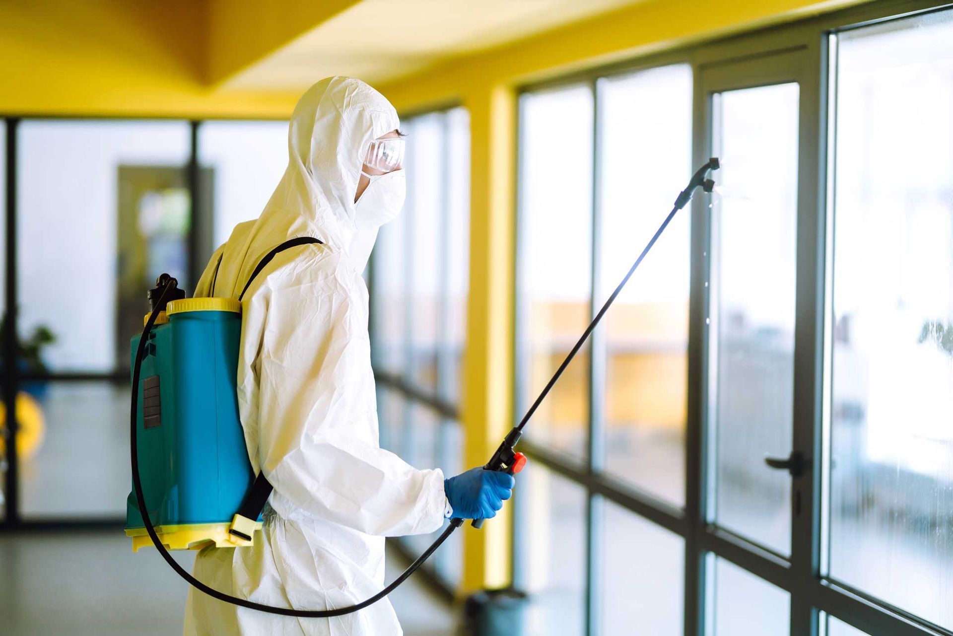 Worker in protective suit spraying disinfectant on glass windows indoors Worker in protective suit spraying disinfectant on glass windows indoors