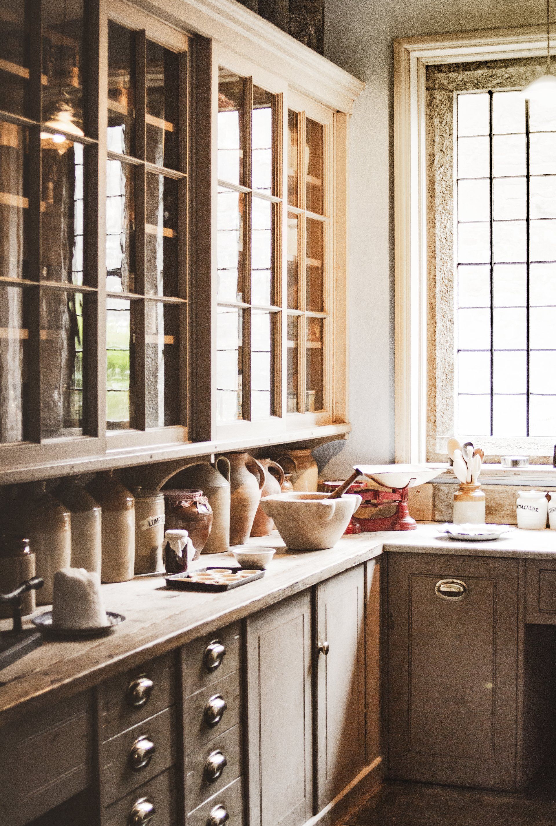 A rustic, well-lit kitchen with wooden cabinetry, glass-paned upper cabinets, and a variety of pottery on the counter.