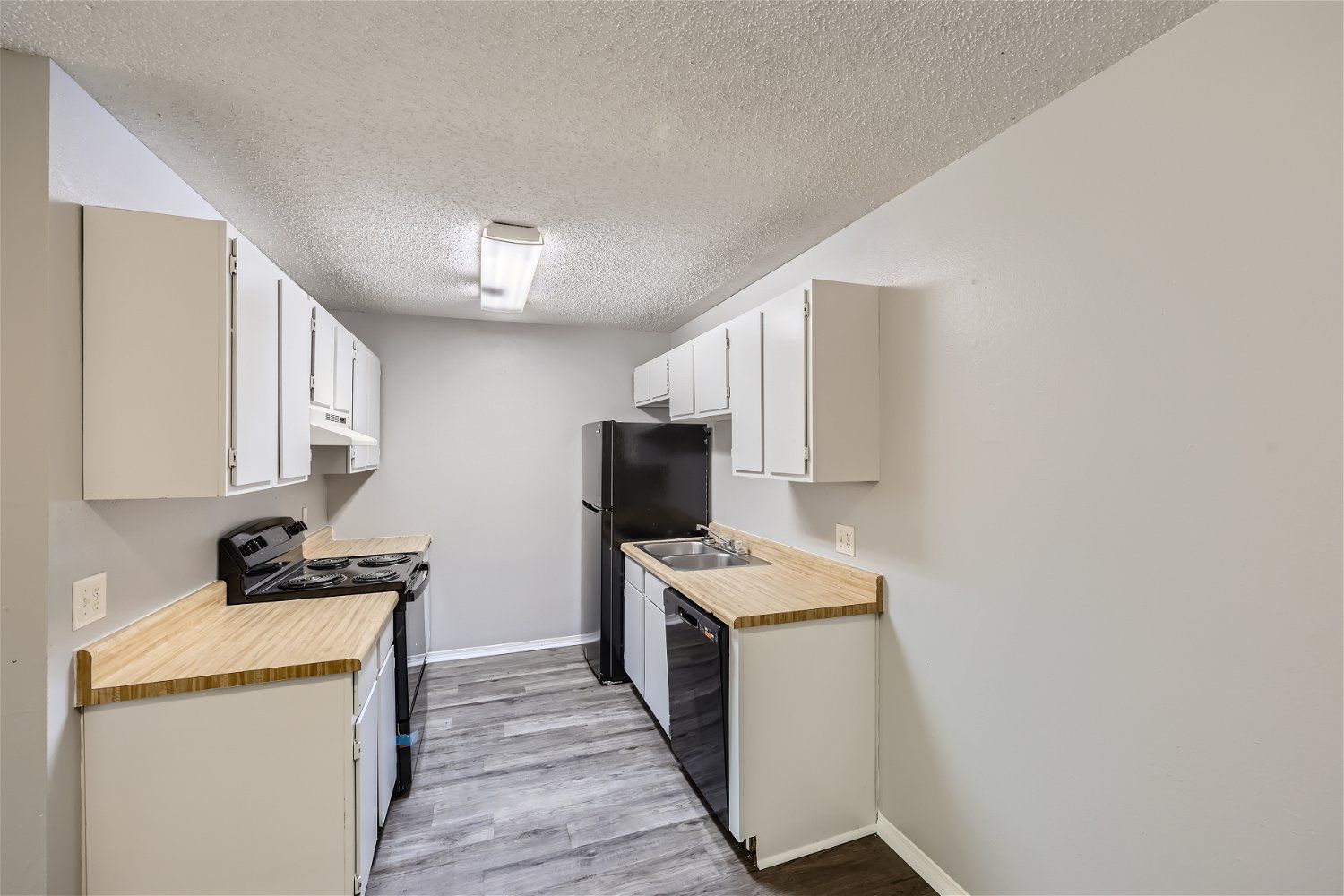 A narrow kitchen with white cabinets, light wood counters, and gray walls. Includes black appliances and light fixture.