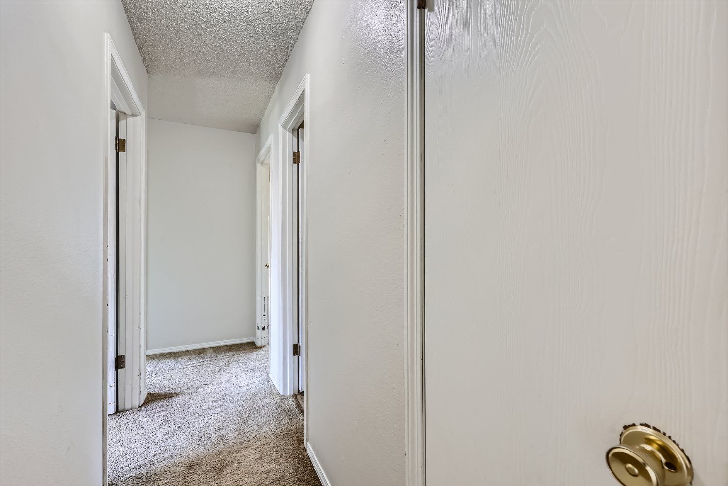 Narrow hallway with white walls and doors, textured ceiling, and worn carpet.