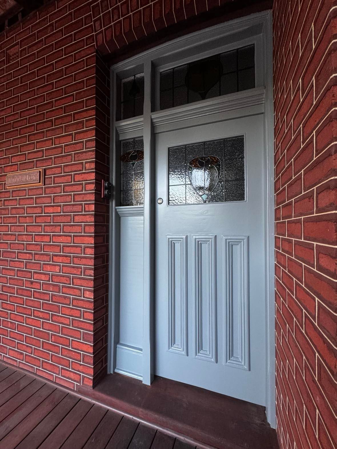 A blue door is sitting on a porch next to a red brick wall.