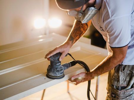 A man wearing a mask is sanding a piece of wood.