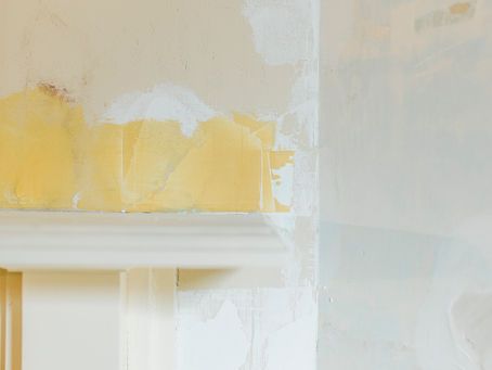 A close up of a wall with peeling wallpaper and a white trim.