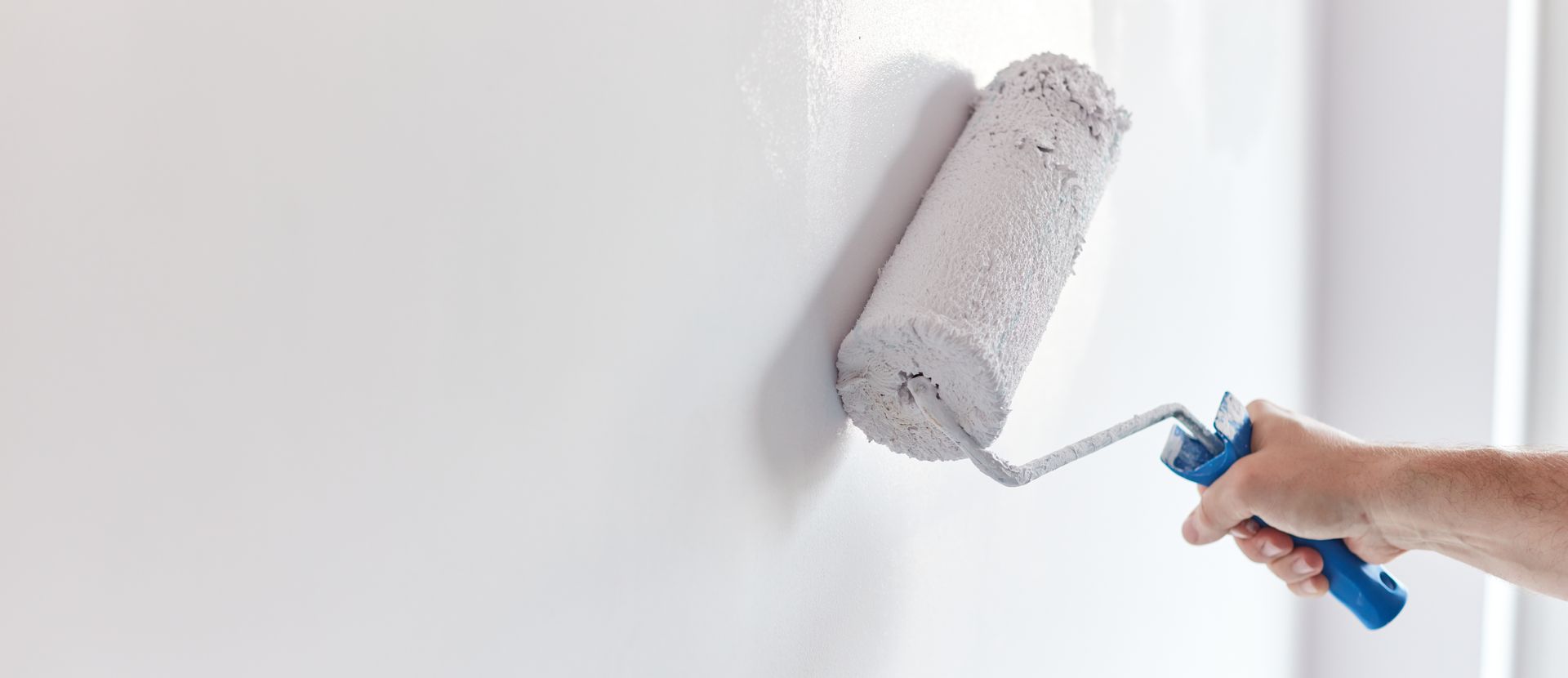 Close-up of a paint roller applying white paint to an interior wall.
