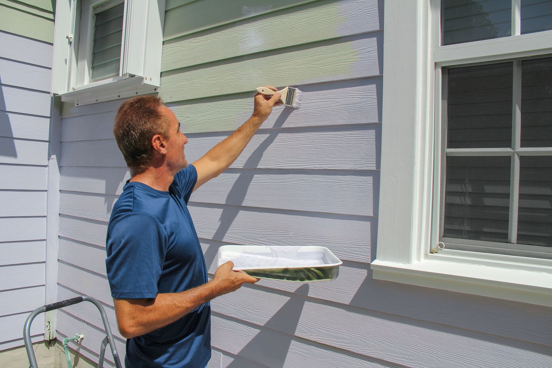 A man using a paintbrush to paint a house exterior, showing residential painters at work.