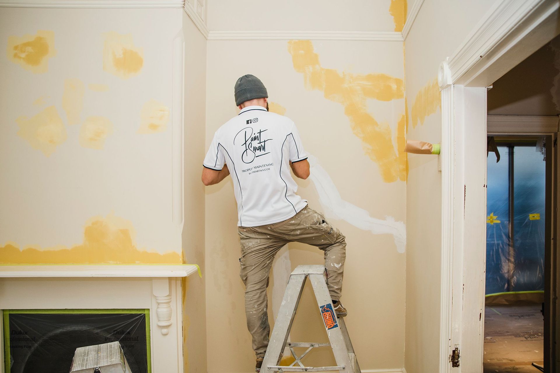 A man is standing on a ladder painting a wall.