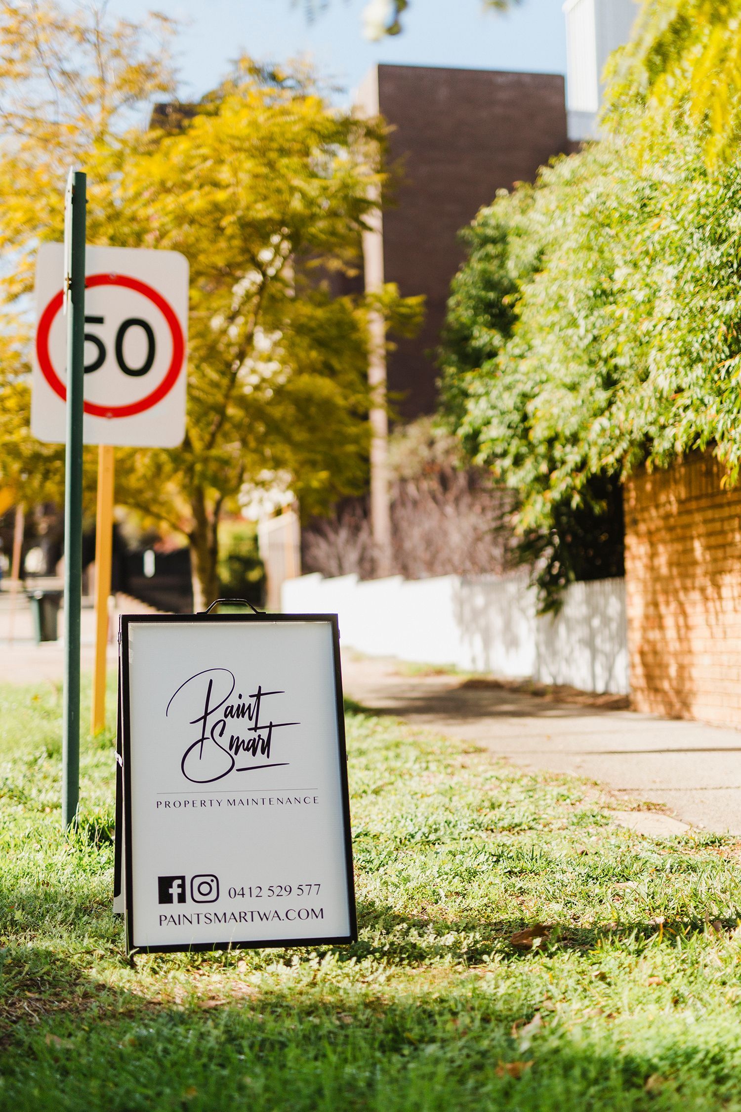 A white sign is sitting in the grass next to a street sign.