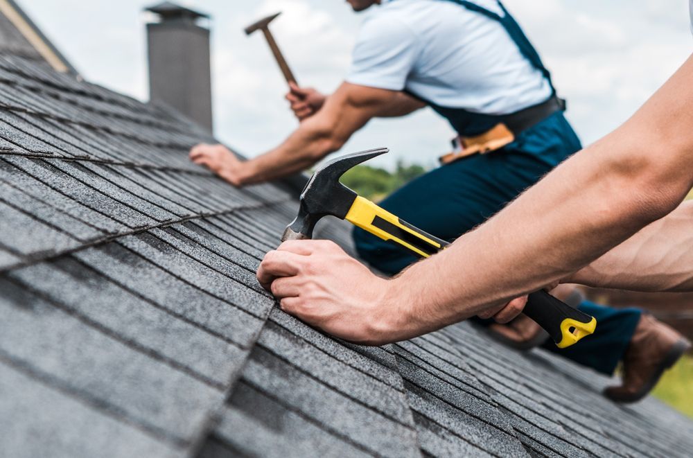 Two men are working on a roof with hammers and nails.