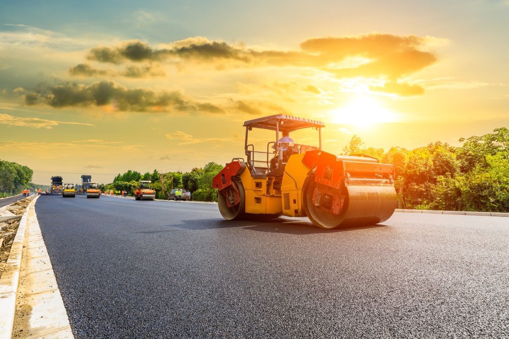 A Roller is Rolling Asphalt on a Highway at Sunset — Rowdraulics NQ Pty Ltd In Mount Louisa, QLD
