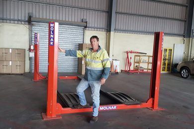 Man Standing Beside Vehicle Hoist — Servicing Hydraulics System in Garbutt, QLD