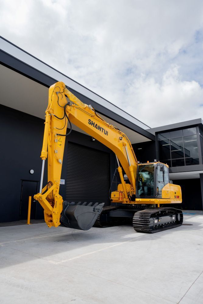A Yellow Excavator is Parked in Front of a Building — Rowdraulics NQ Pty Ltd in Mount Louisa, QLD