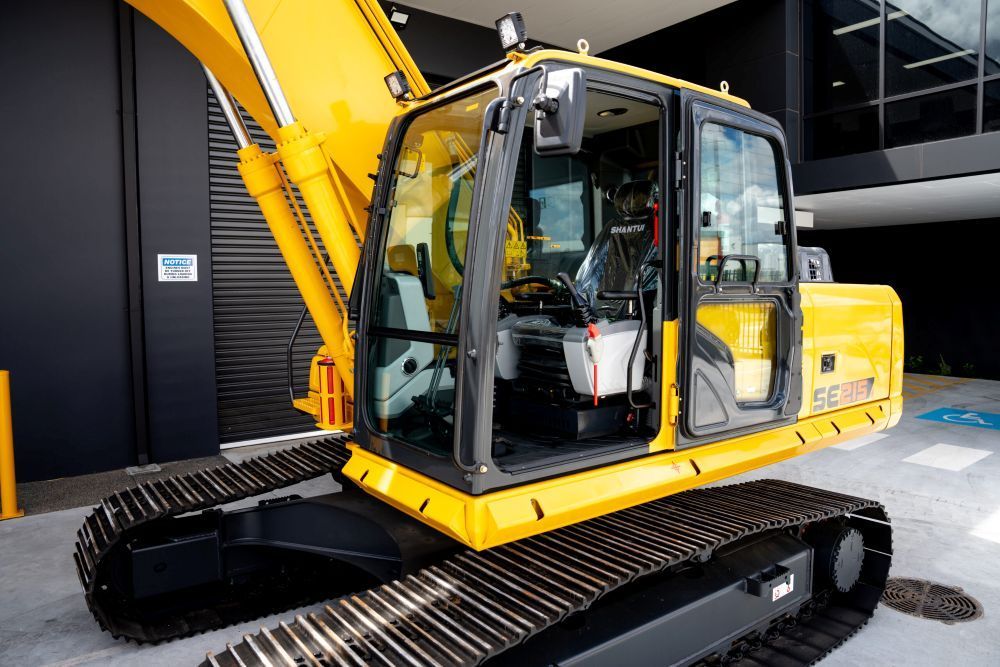 A Yellow Excavator is Parked in Front of a Building — Rowdraulics NQ Pty Ltd in Mount Louisa, QLD