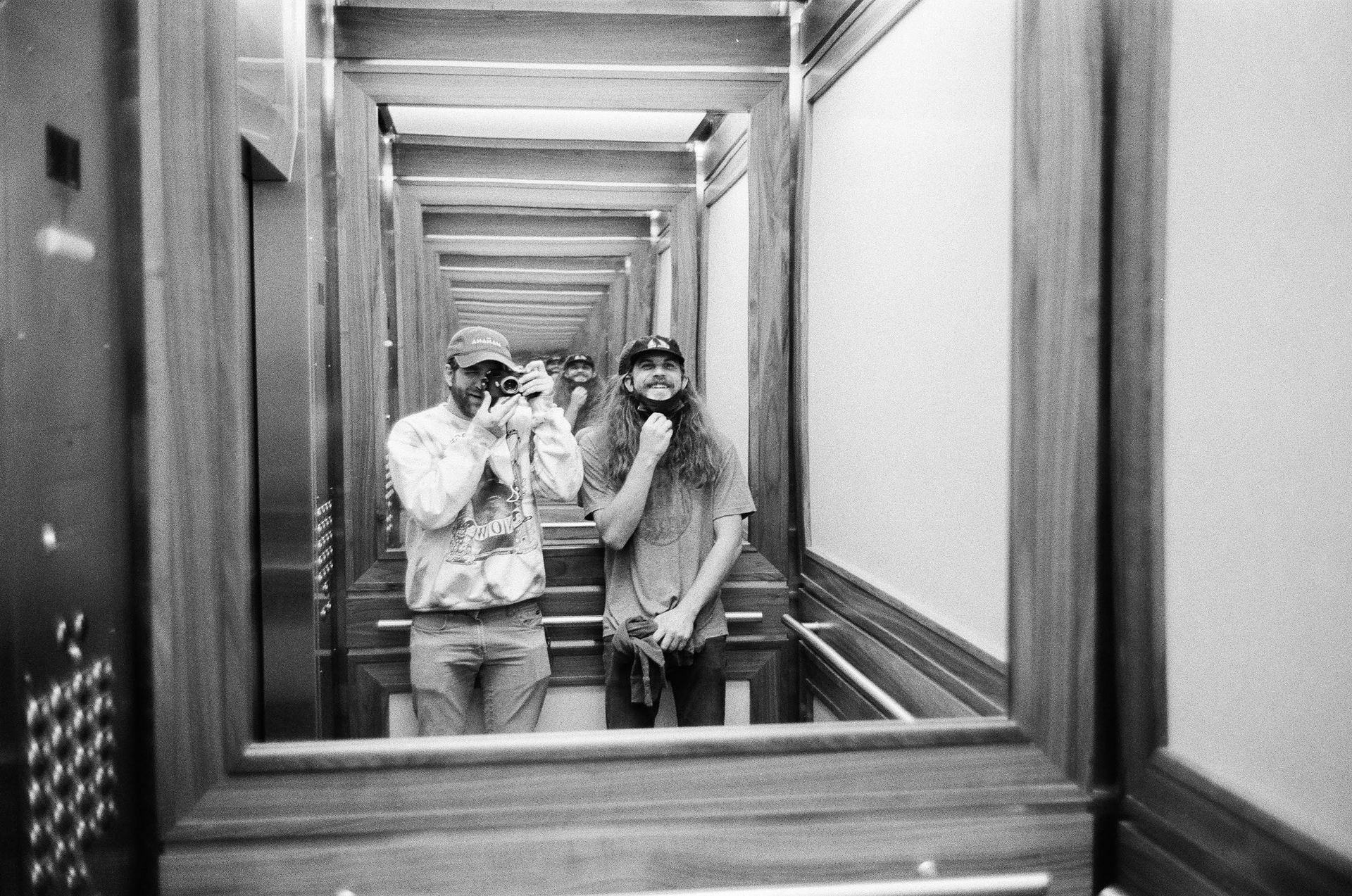 Two men are taking a picture of themselves in an elevator.