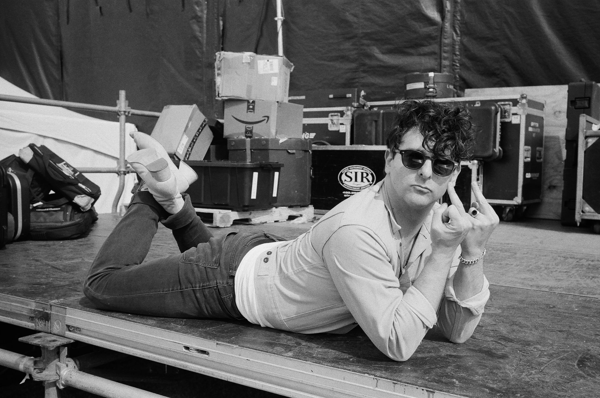 Man laying on a concert stage in sunglasses and looking relaxed.