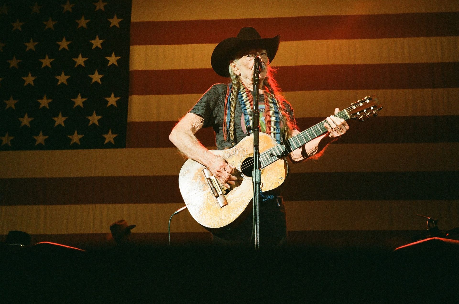 A man in a cowboy hat is playing a guitar in front of an american flag