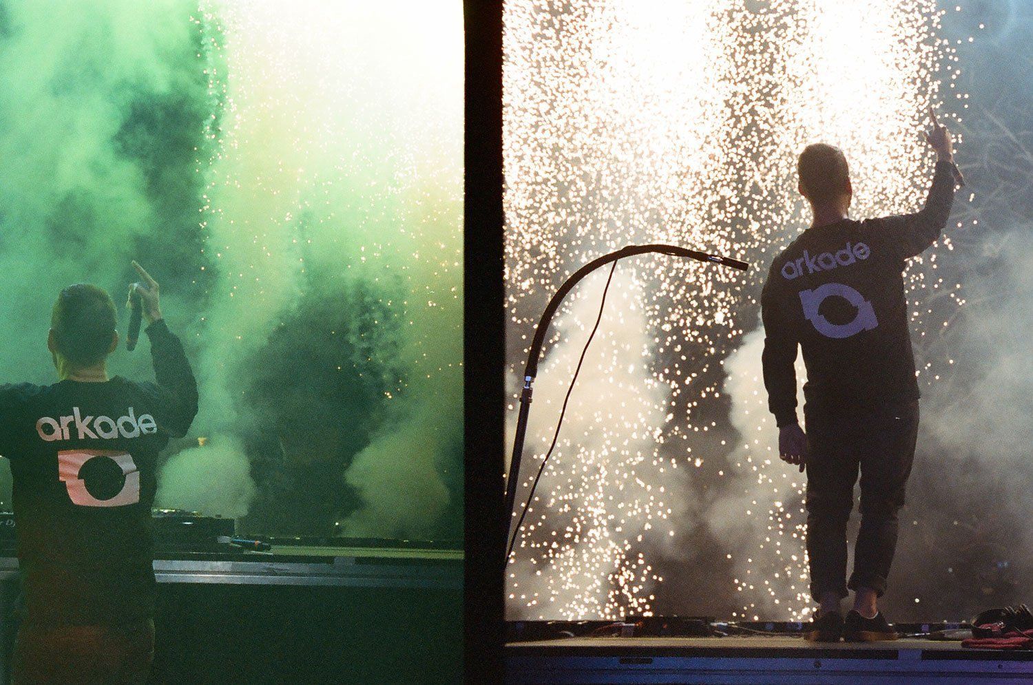 A man wearing an arkadia shirt stands in front of a fireworks display