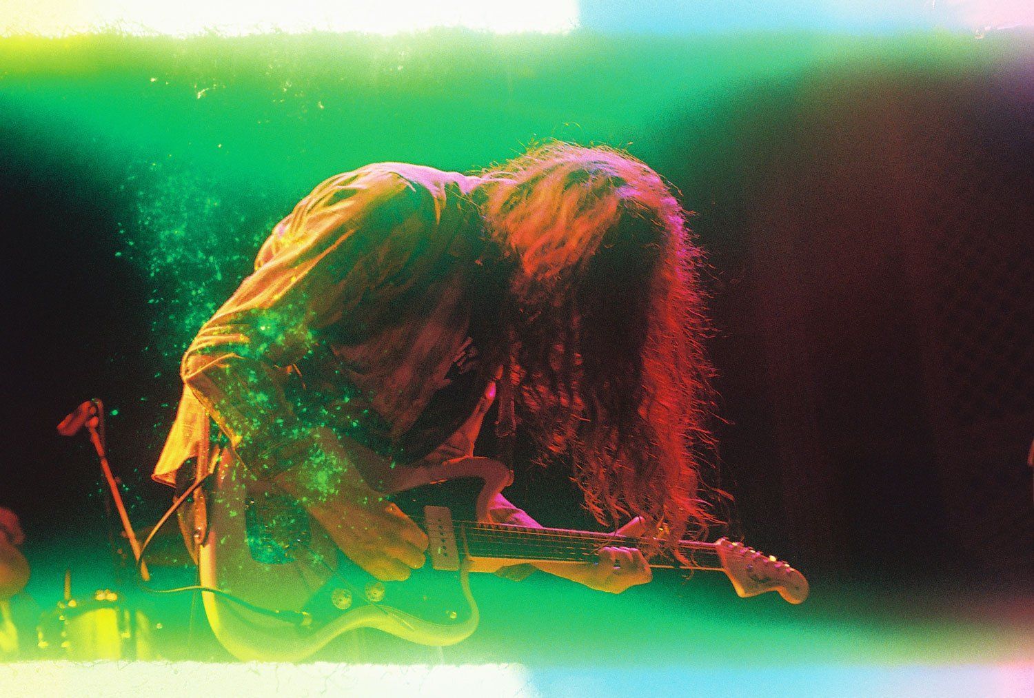 A man with long hair is playing a guitar on a stage.