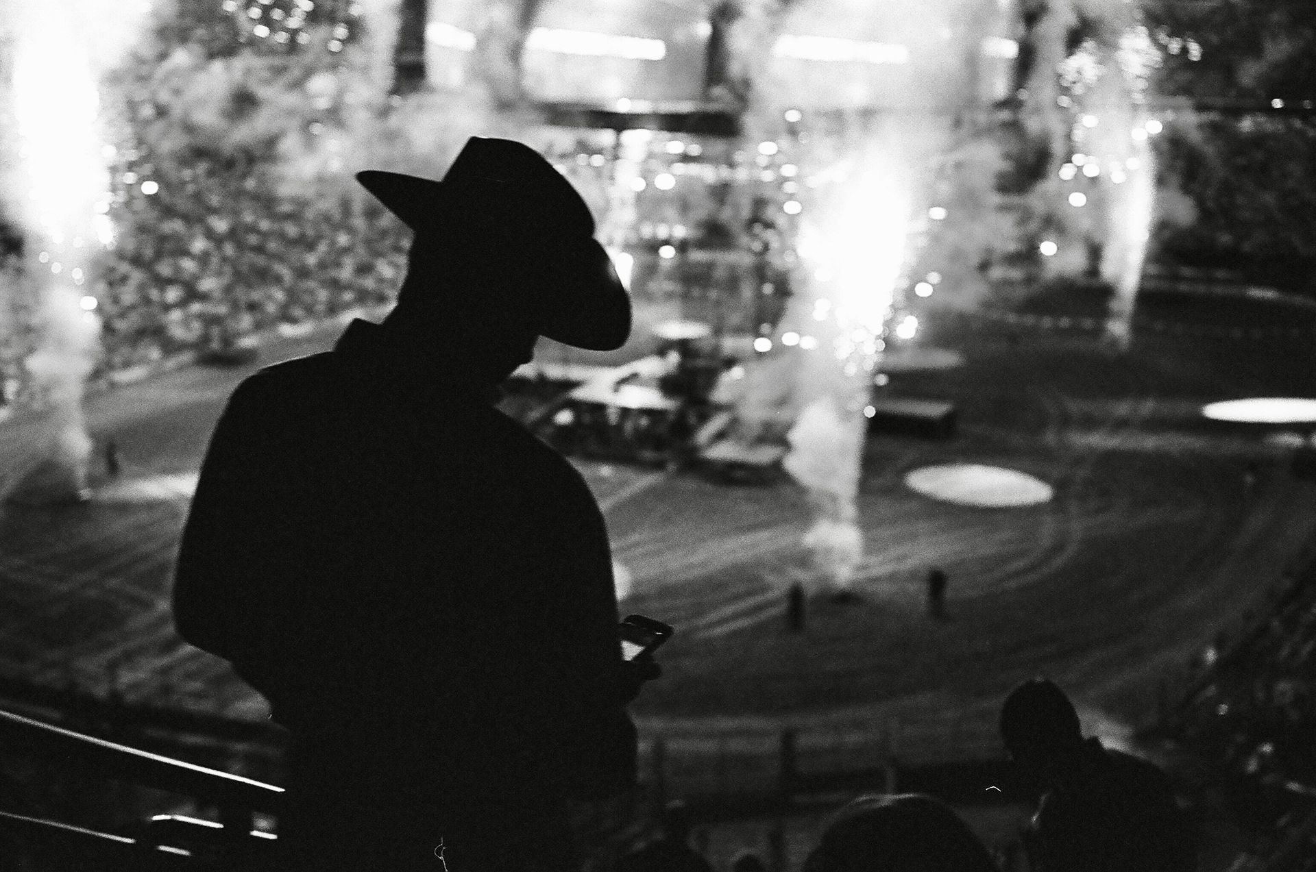 A man in a cowboy hat is standing in front of a fireworks display.
