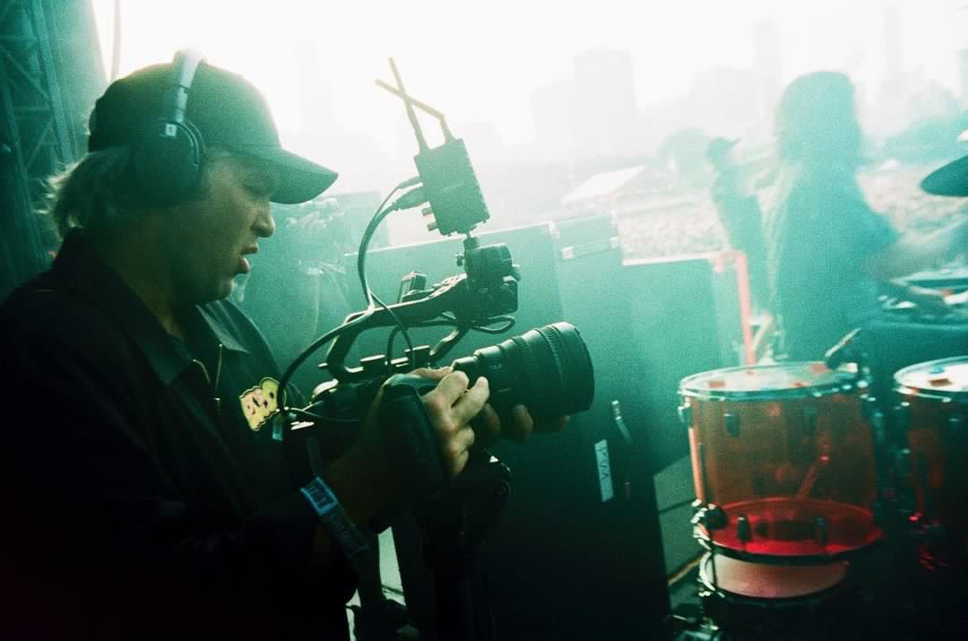 A man is holding a camera in front of a drum set.