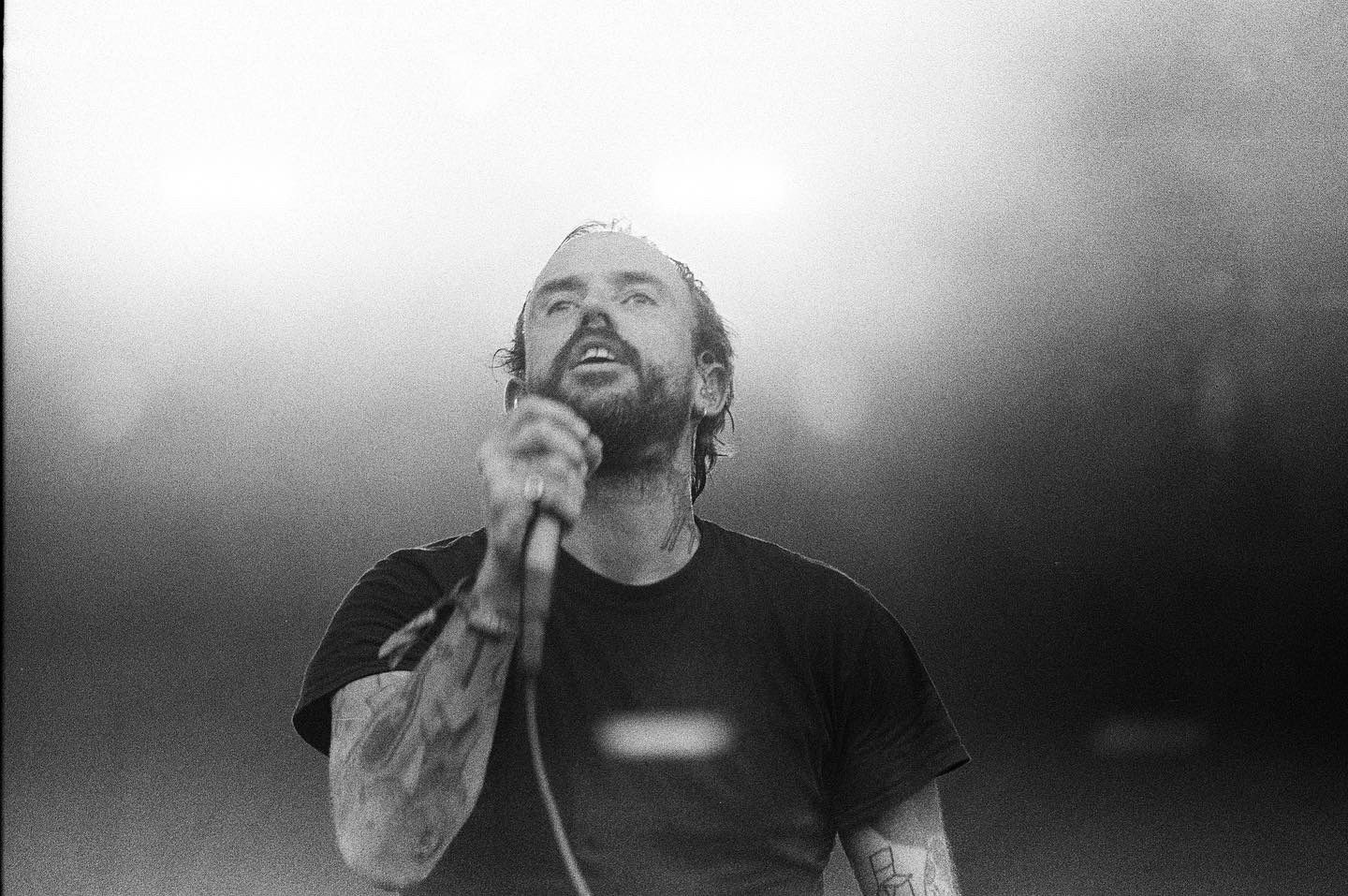 A man with a beard is singing into a microphone in a black and white photo.