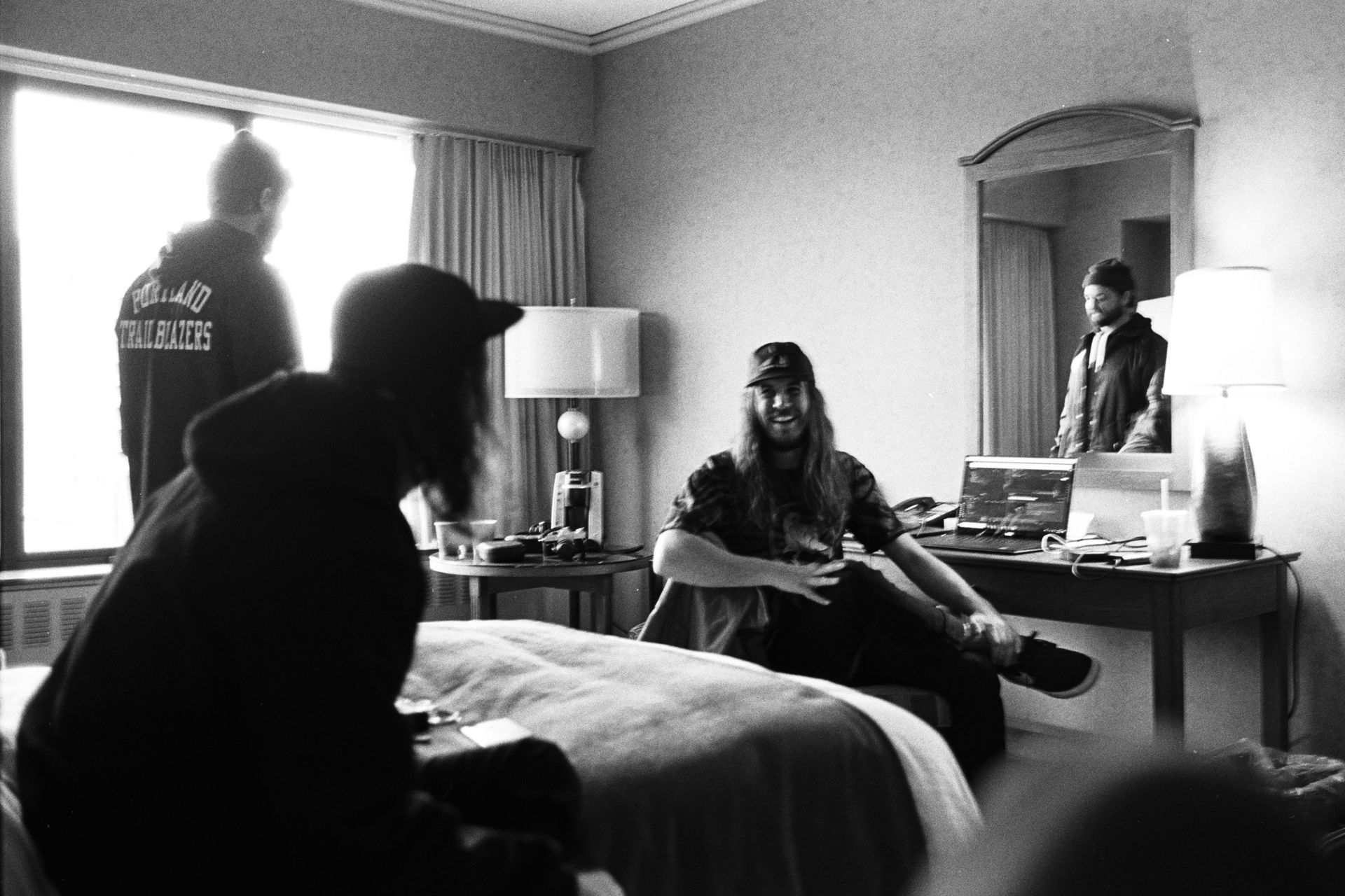 A group of men are sitting on a bed in a hotel room.