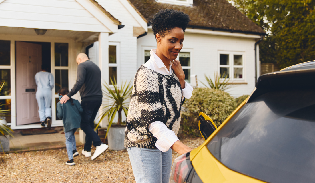 A woman is loading a yellow car in front of a house.