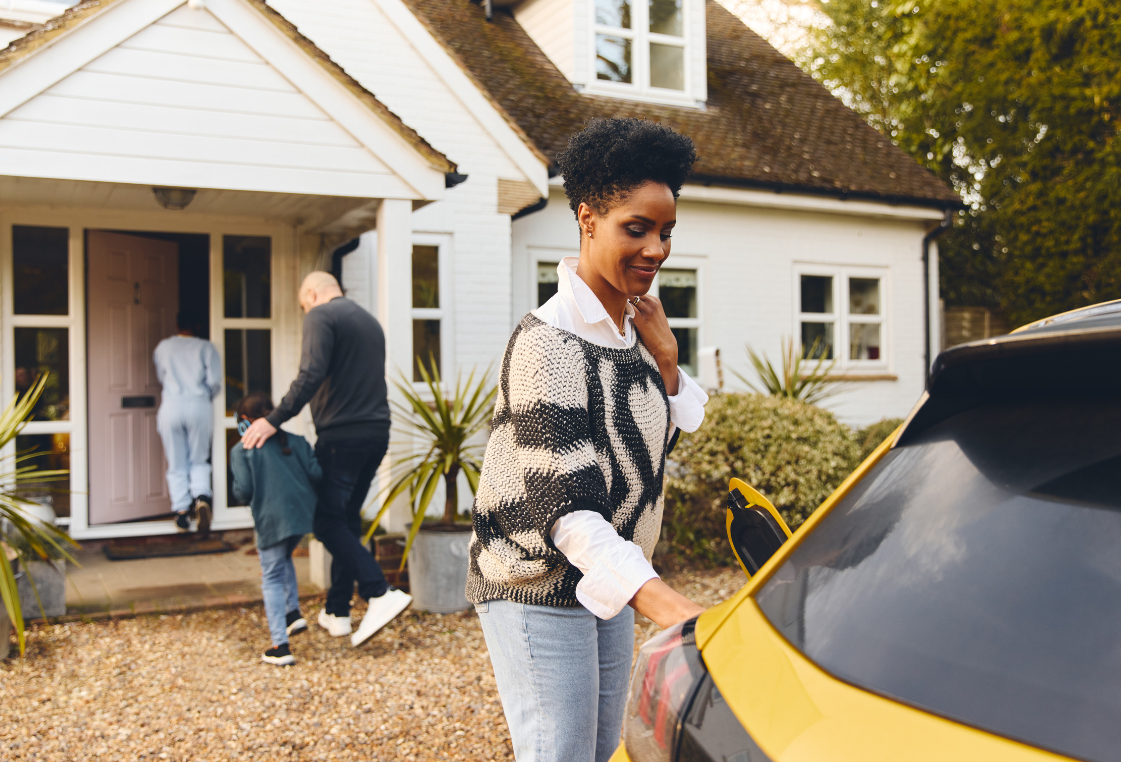 A woman is loading a car in front of a house.