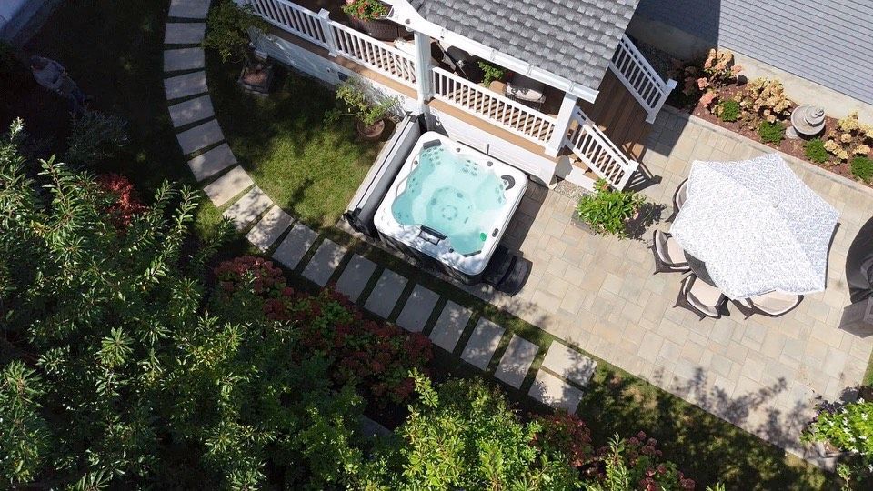 Aerial view of a hot tub next to a gazebo and patio, surrounded by landscaping and greenery.