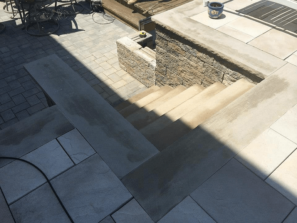 Stone steps and patio with tan and gray tiles. A retaining wall is visible.
