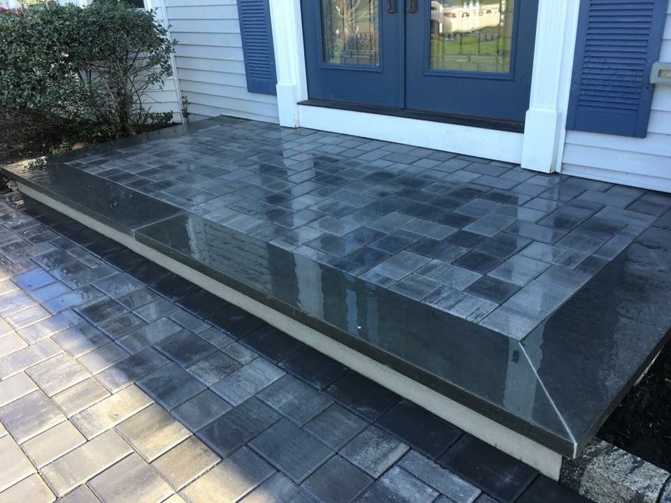 Gray brick steps leading to a blue door with blue shutters on a house.