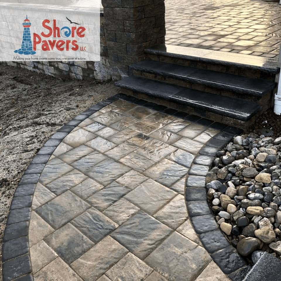 Brick paver pathway with black edging, stairs, and decorative stone.