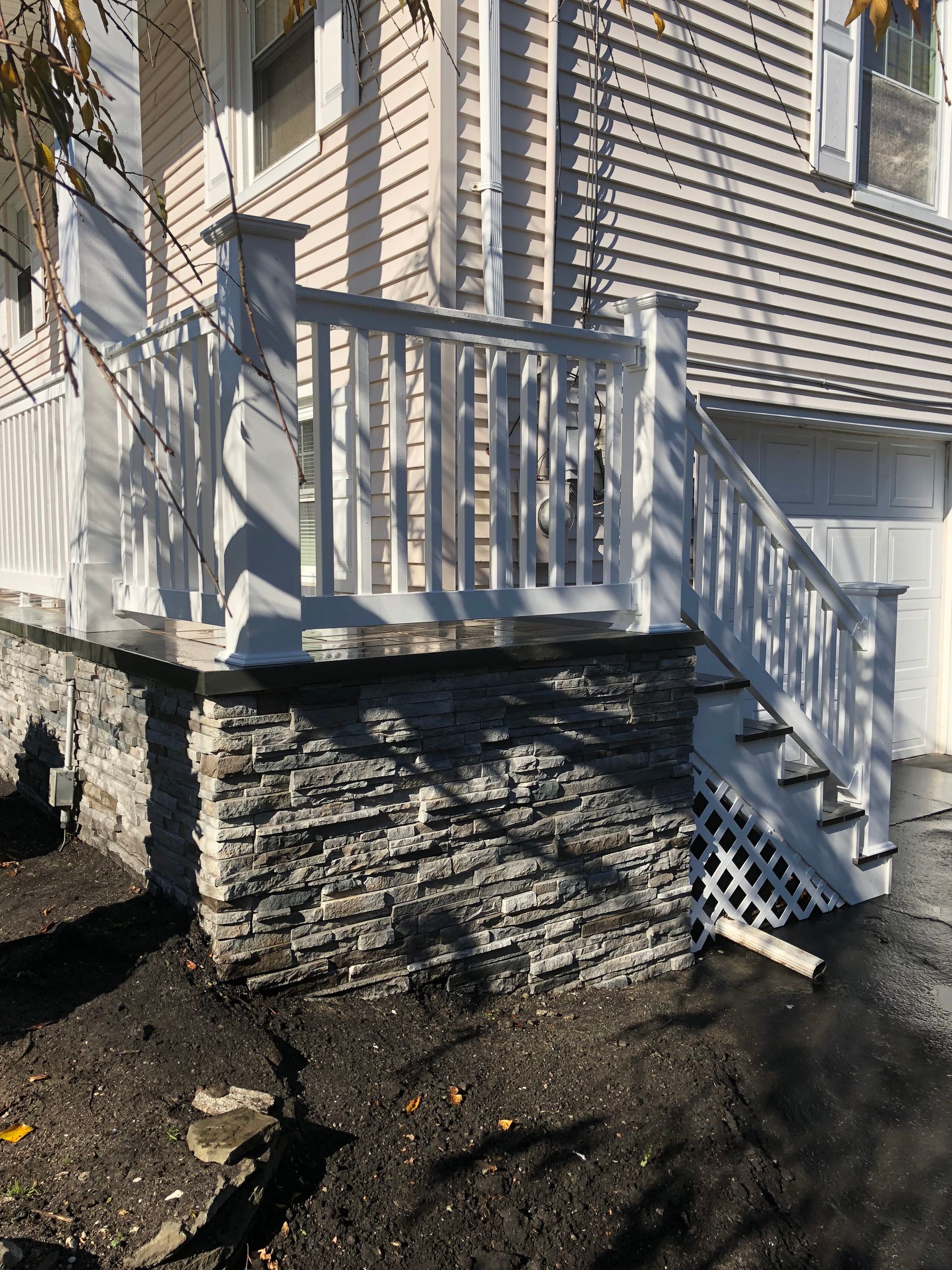 White deck with stairs, stone foundation, and a white house in the background.