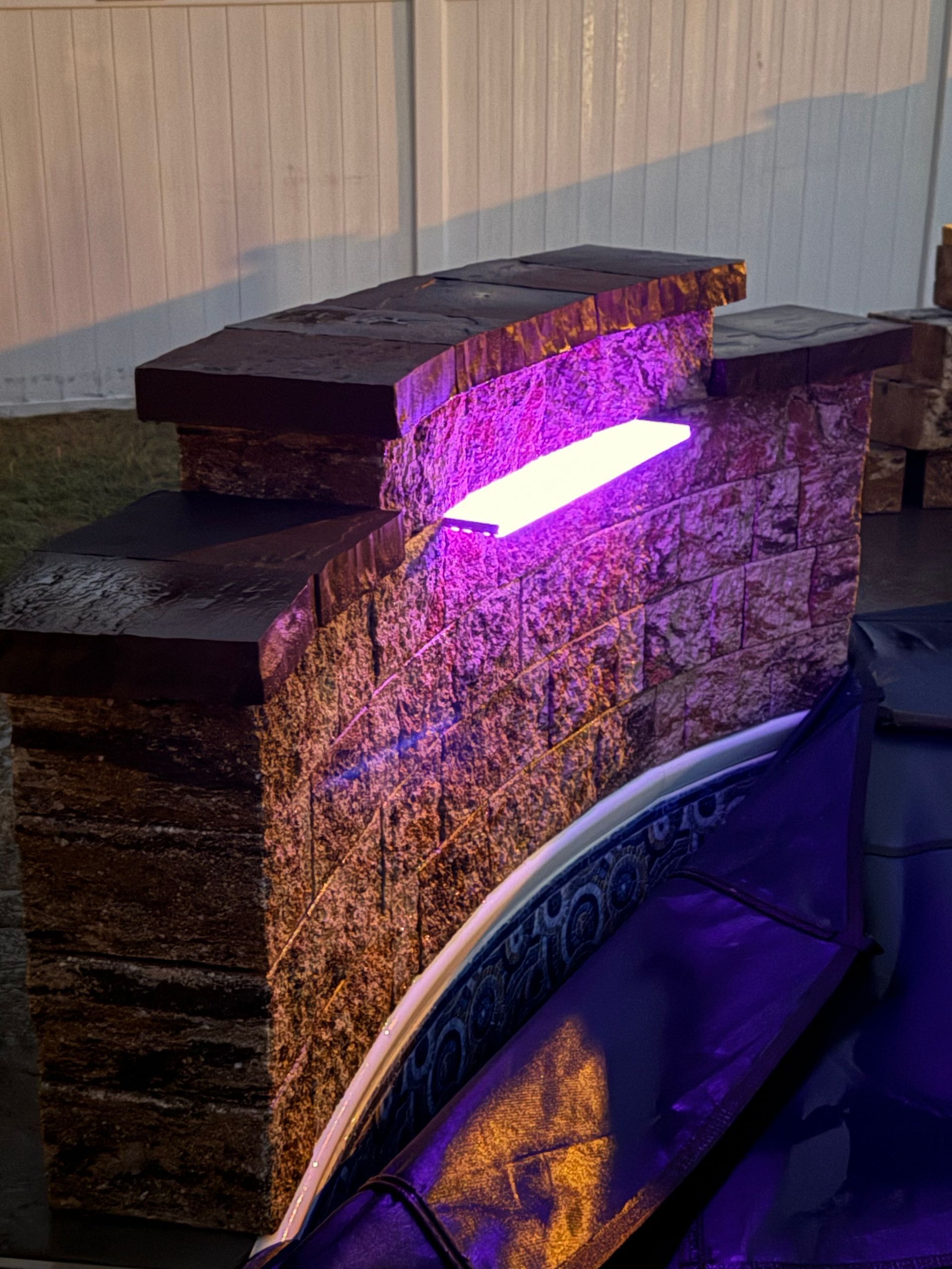 Stone structure with a purple illuminated light, near a pool.