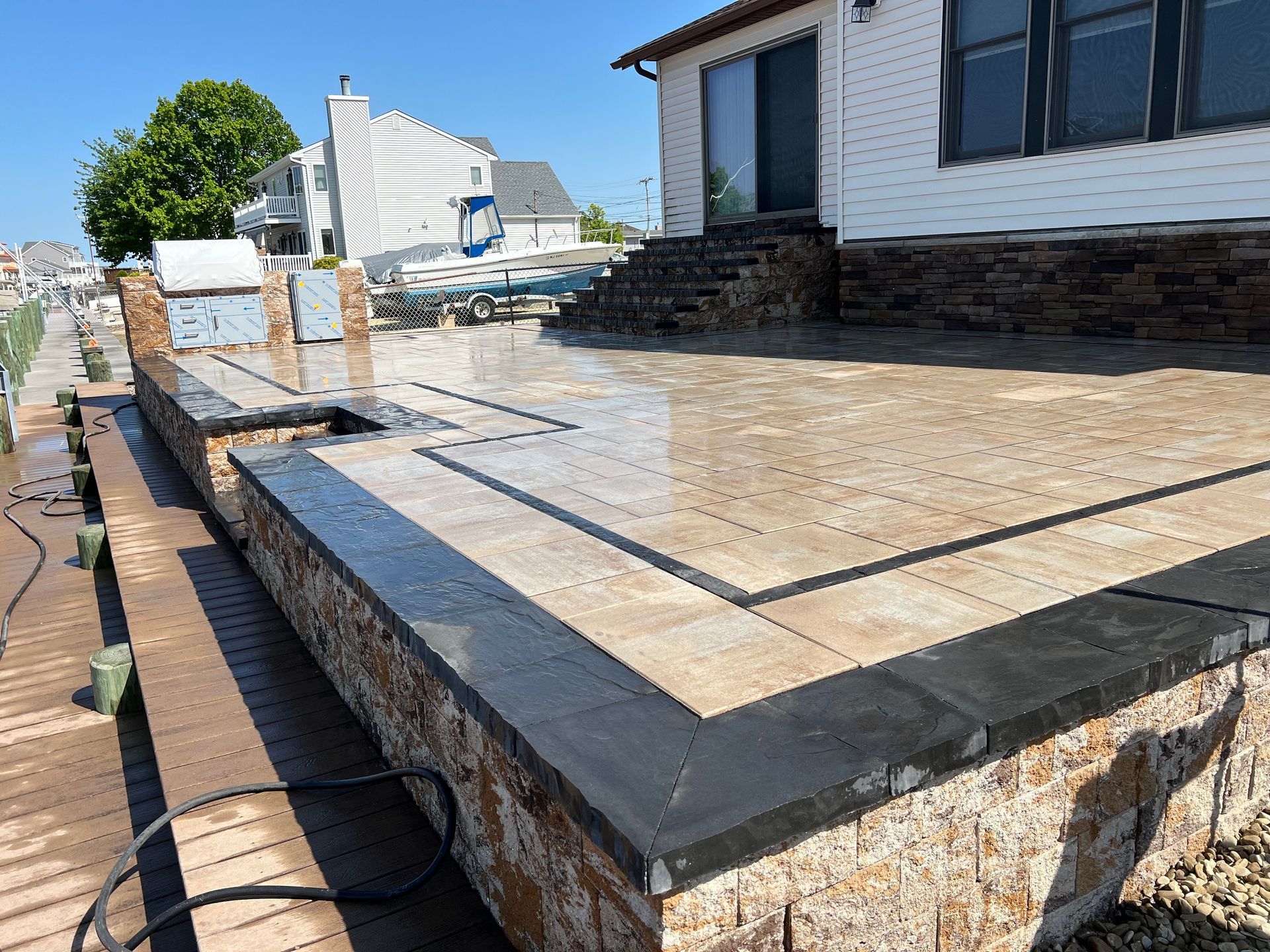 Outdoor patio with stone pavers, black border, and built-in grill near a waterway.