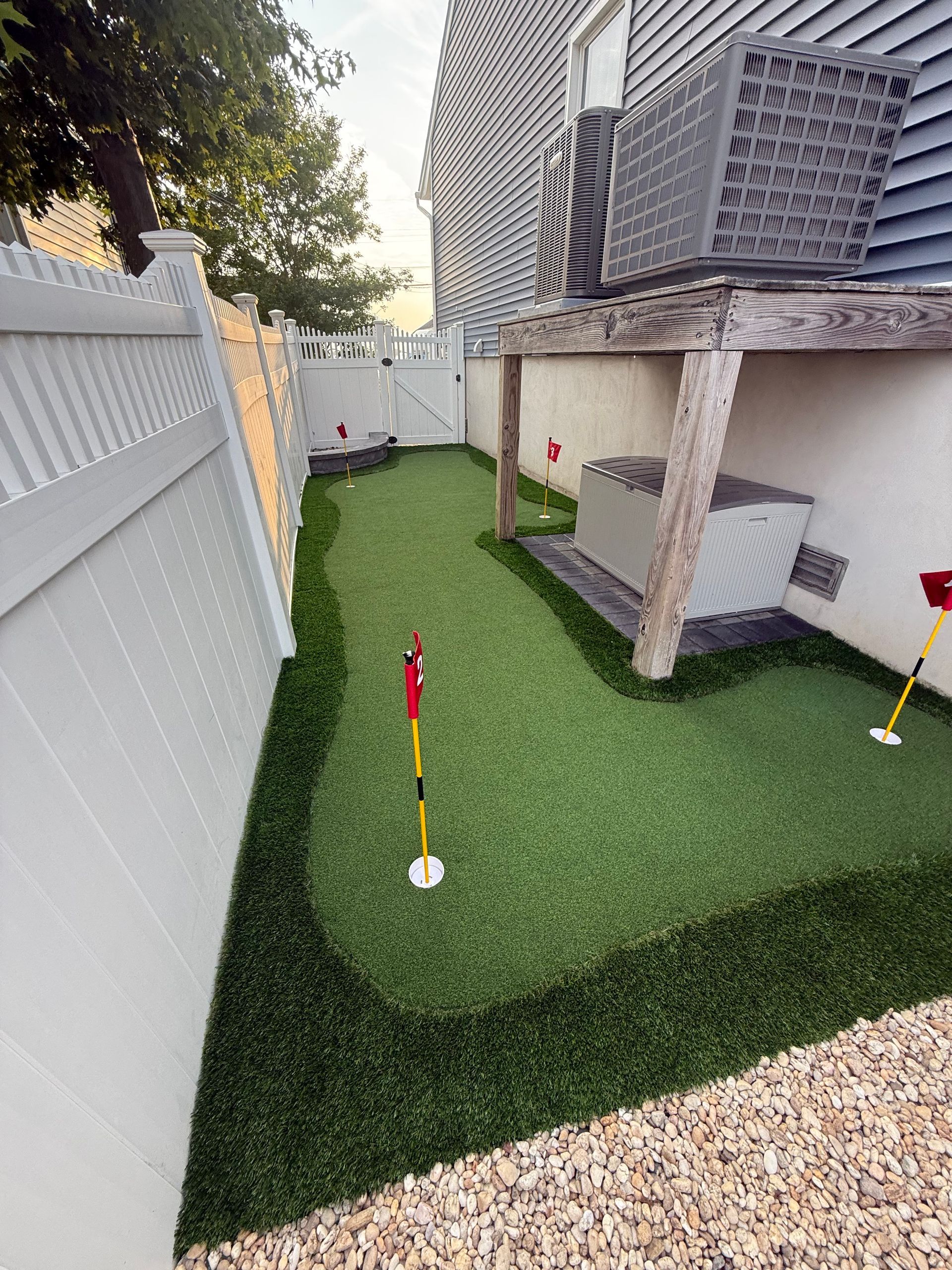 Backyard putting green with white fence, red flags, and artificial turf.