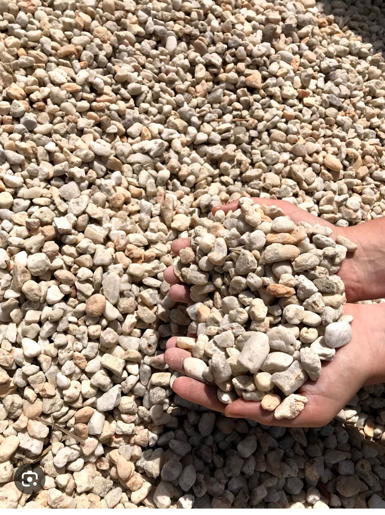 Hands holding a pile of beige and tan river rock against a backdrop of more rock.