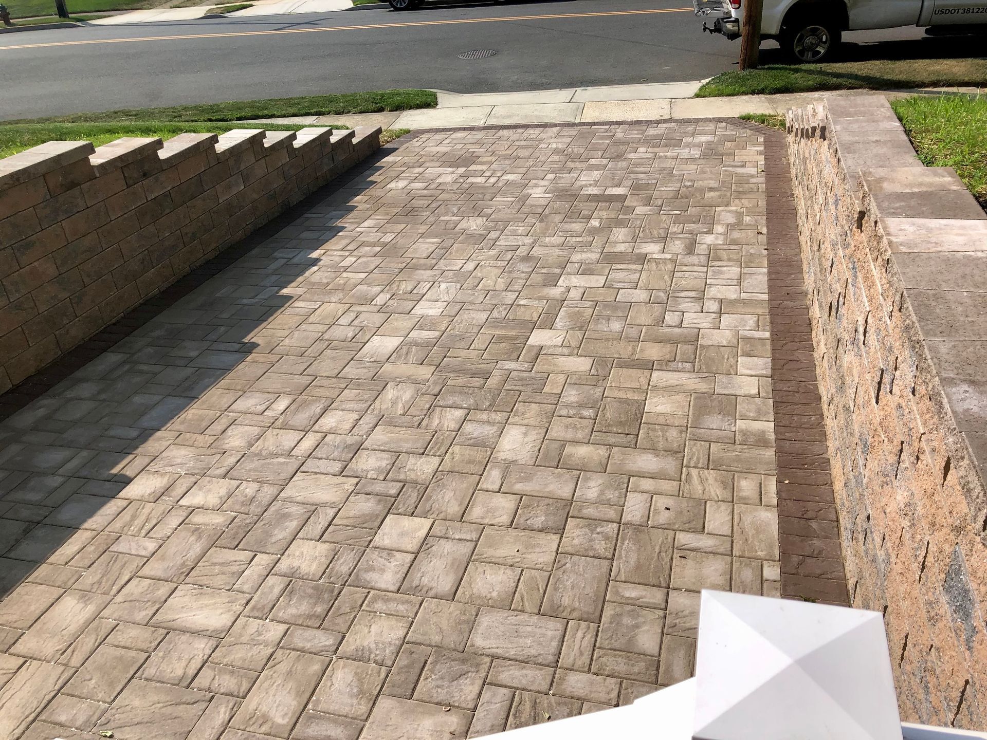 Brick driveway with low brick walls on both sides. A white post is in the foreground.