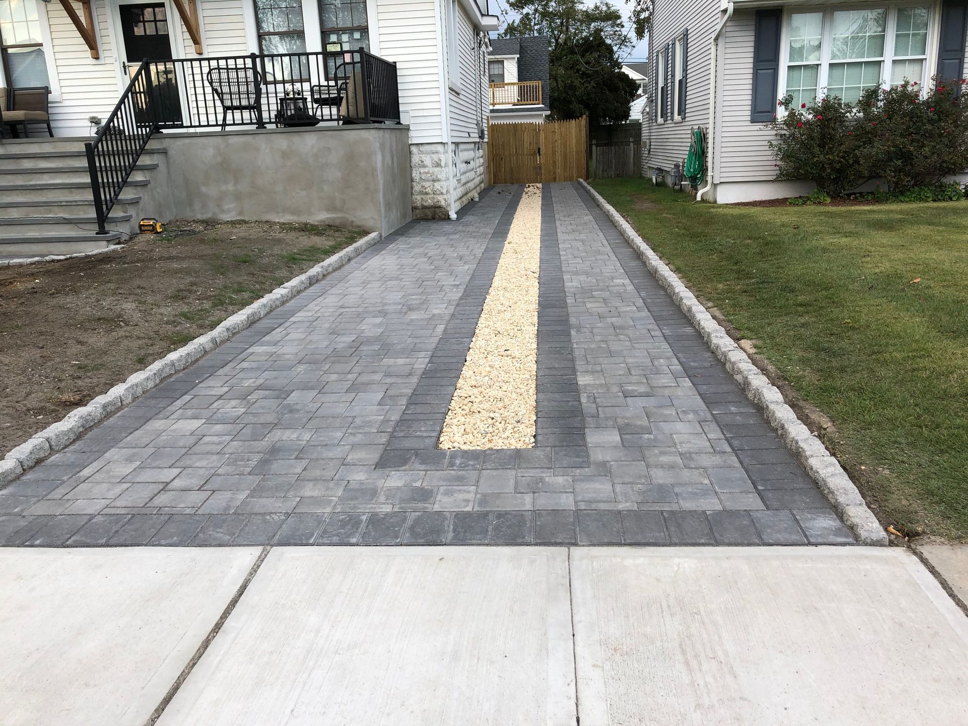 Driveway paved with gray bricks and a central strip of yellow gravel, leading to a house.