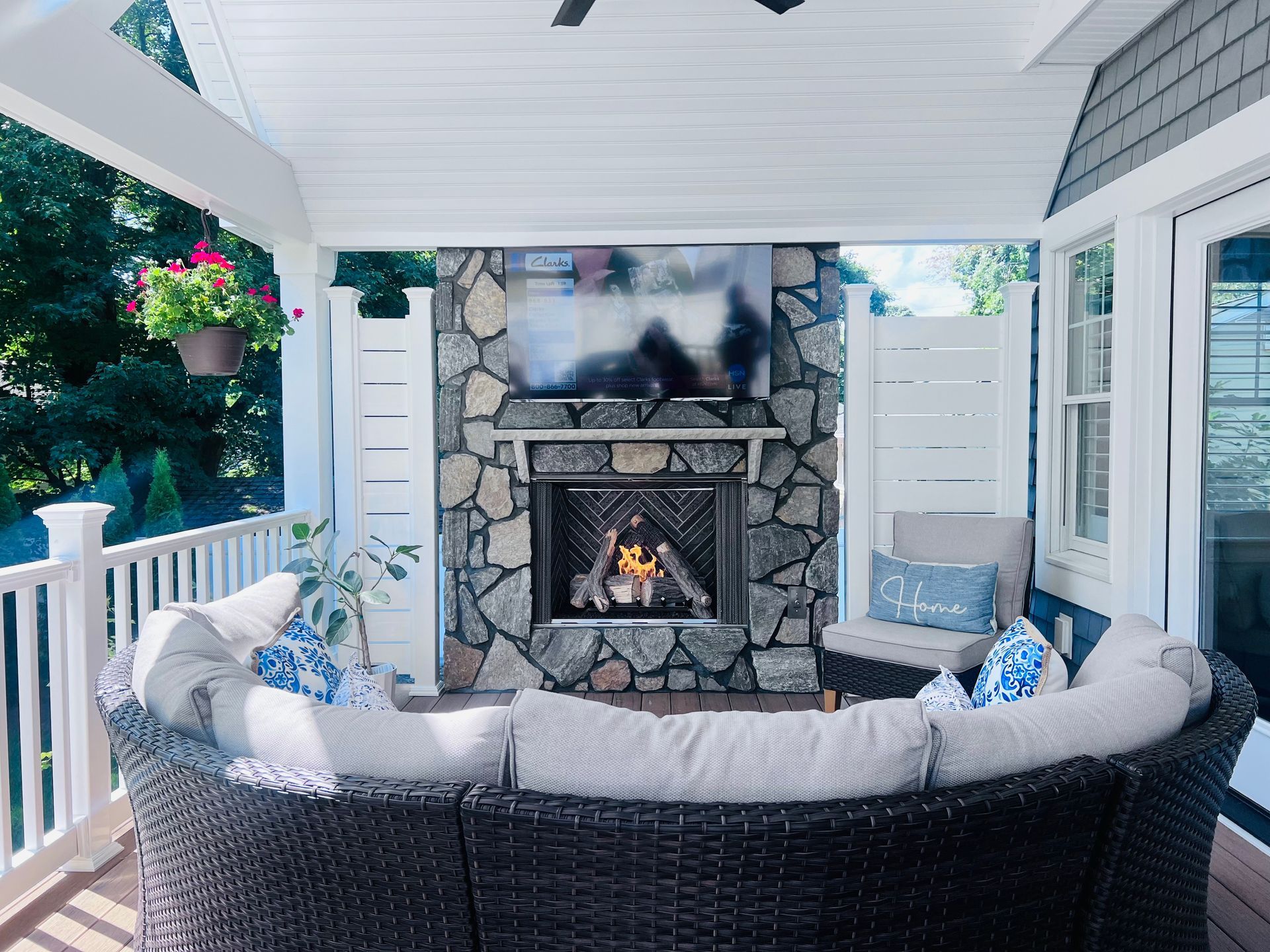 Outdoor living space with stone fireplace, TV, and curved wicker sectional.