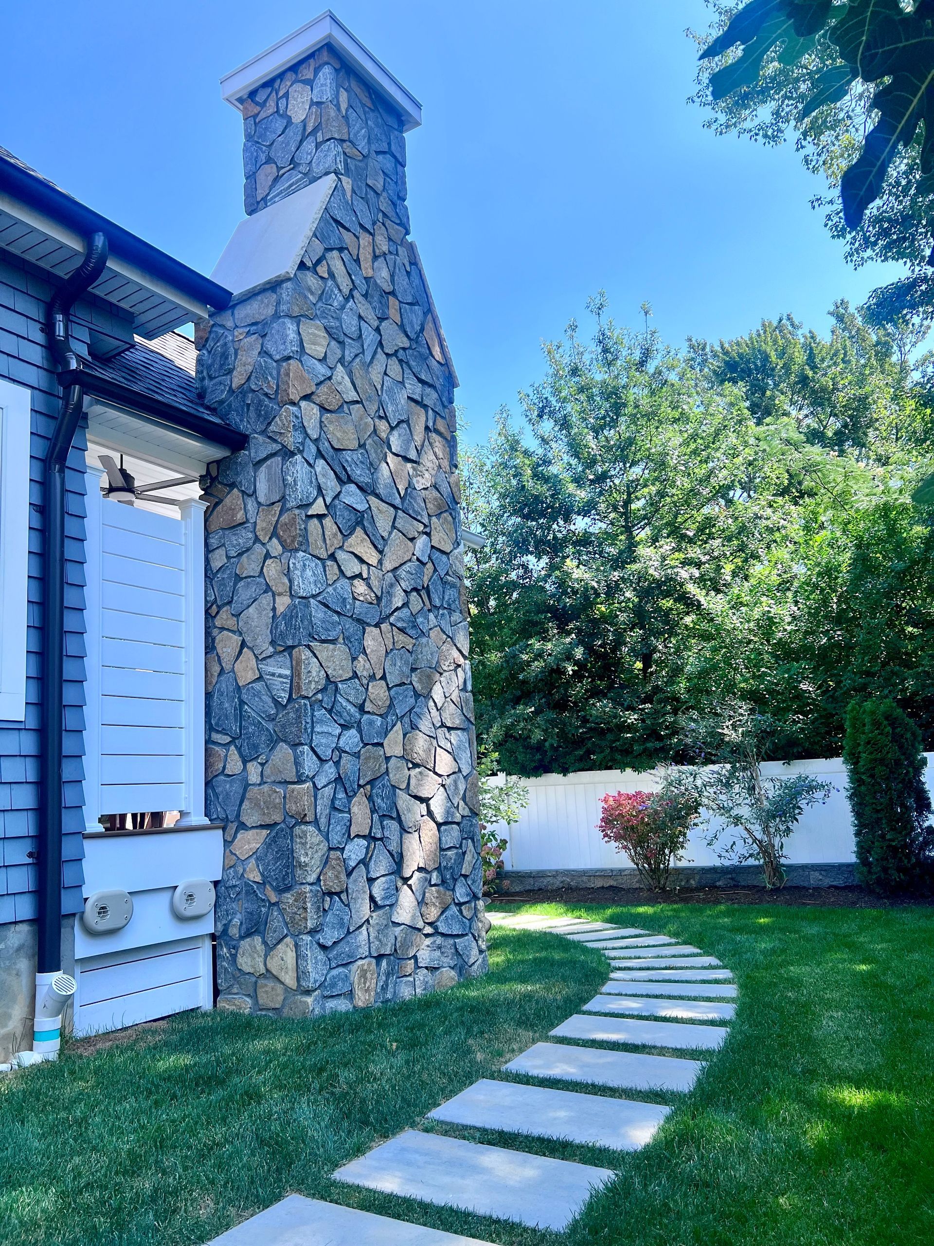 Stone chimney next to a blue house, a stone path through a green lawn.