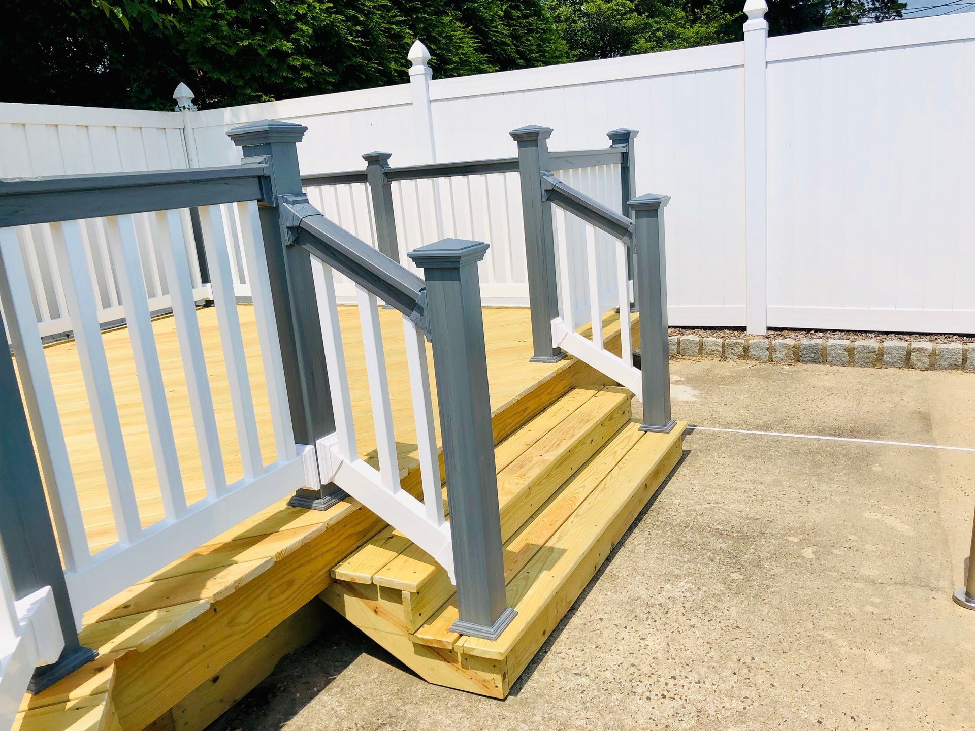 Wooden deck with gray and white railings, steps, and white fence in the background.